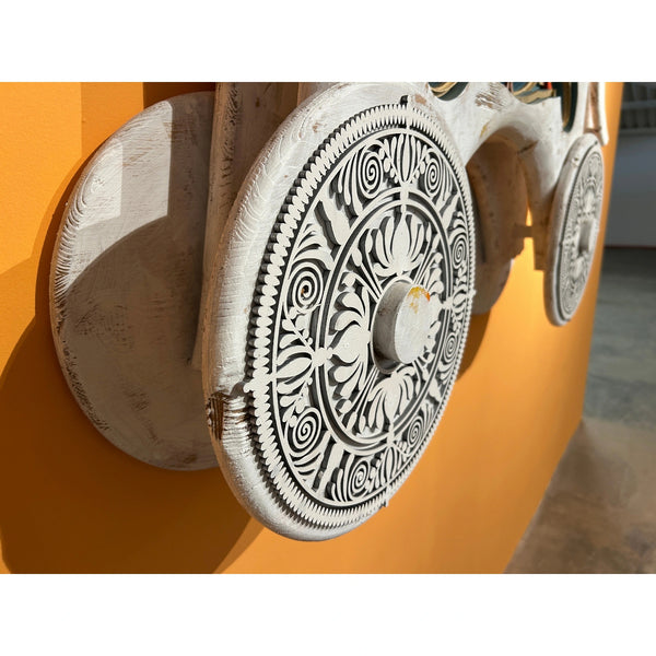 Close-up detail of hand-carved wooden wheel with intricate patterns on Mário Belém sculpture
